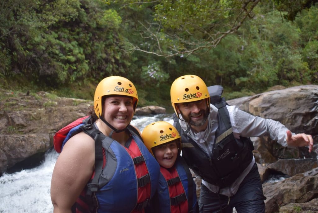 Mãe e filho americanos abraçando o guia de turismo Rocco Belletti com equipamento de segurança para rafting na frente do Rio Capivari